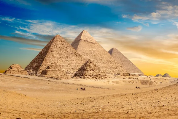 The three pyramids of Giza rising from the desert plateau with camels in the foreground at sunset