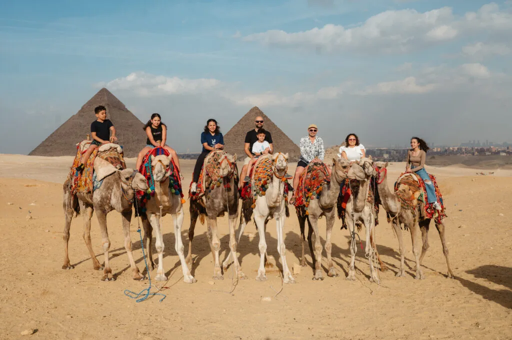 Family group on camel safari at Giza Pyramids with Pyramid of Khafre and Pyramid of Menkaure desert panorama Cairo Egypt