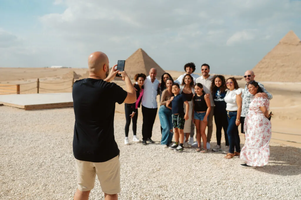 Tourist photographing family group at Giza Pyramids panoramic viewpoint with Pyramid of Khafre and Pyramid of Khufu background Cairo Egypt