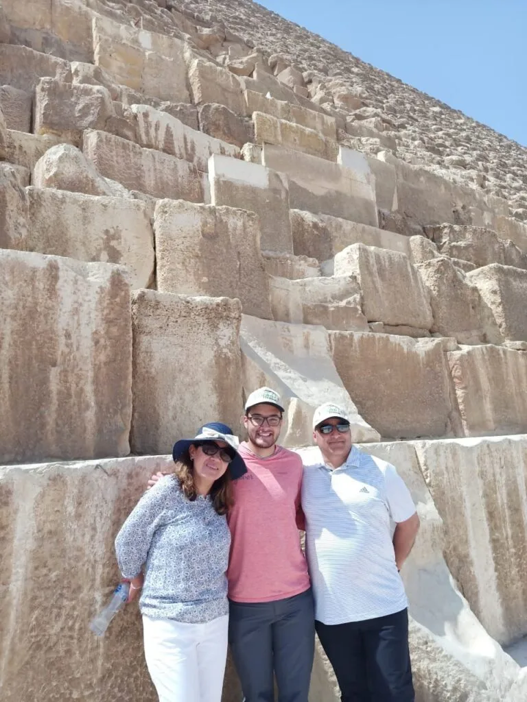 Empire Travel tourists wearing branded caps posing at base of Great Pyramid of Khufu massive limestone blocks Giza Egypt