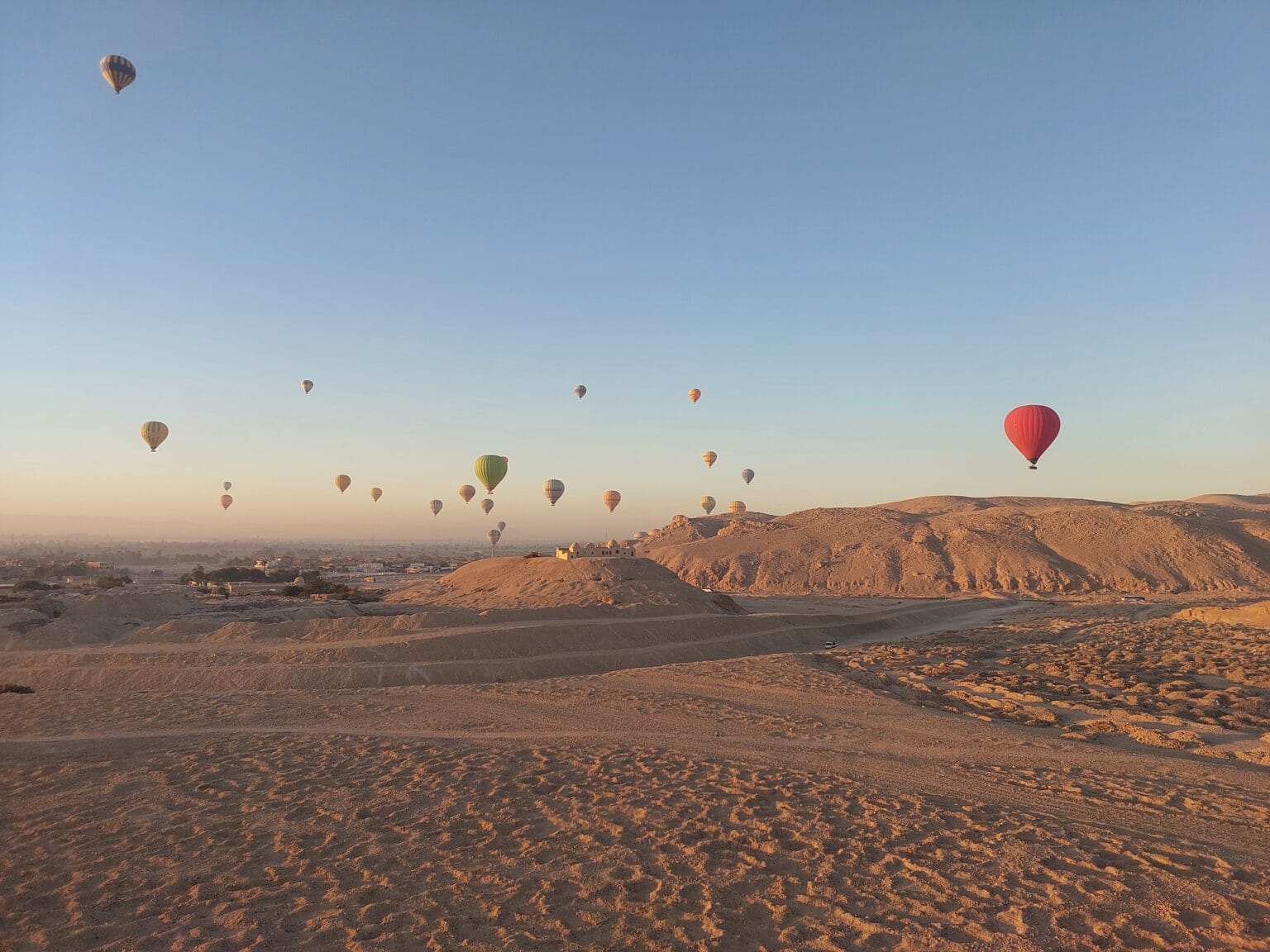 Hot air balloons flying over Luxor West Bank at sunrise above the ancient desert landscape in Egypt
