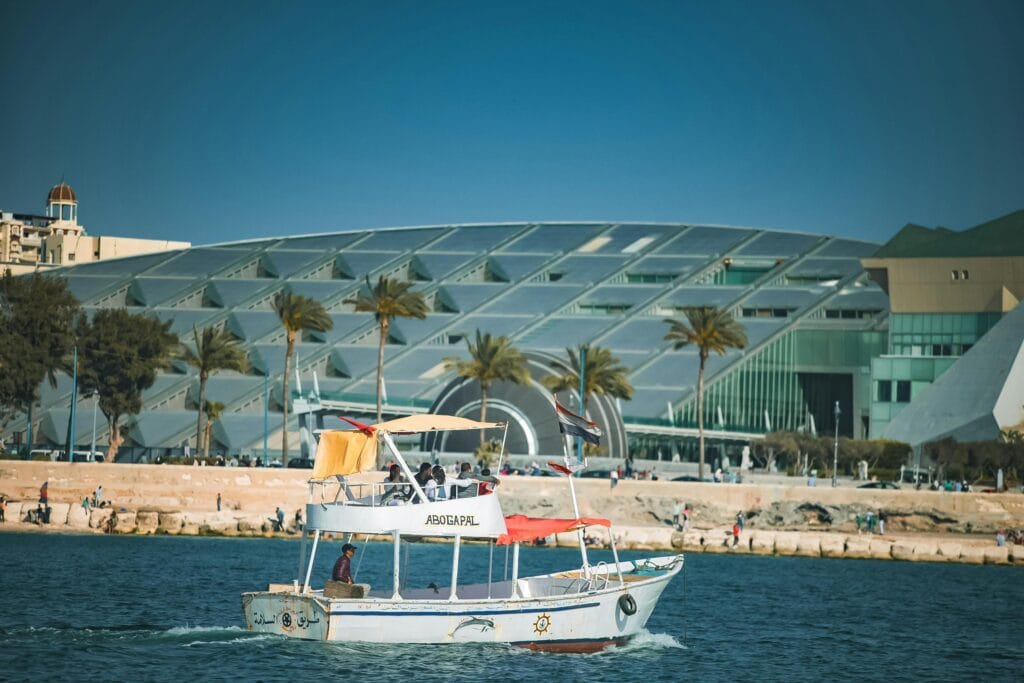 Small boat sailing in front of the Bibliotheca Alexandrina, the modern Library of Alexandria, on the Mediterranean coast of Alexandria, Egypt.