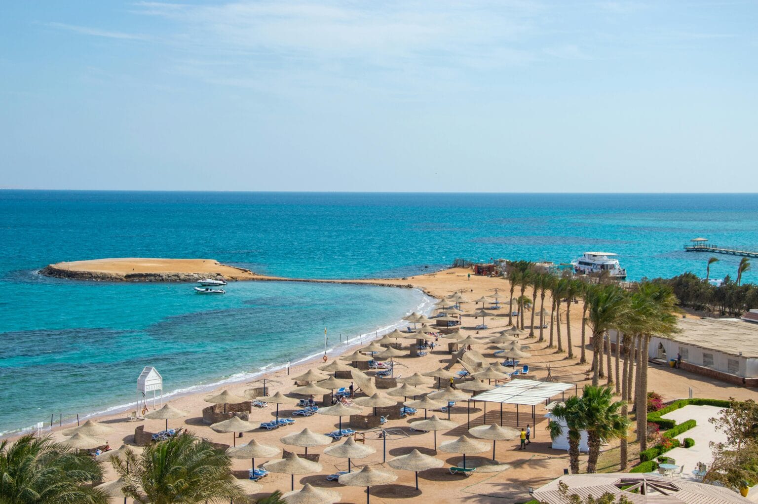 Beach resort in Hurghada Egypt with palm trees, sun umbrellas, and turquoise Red Sea water along the coastline.