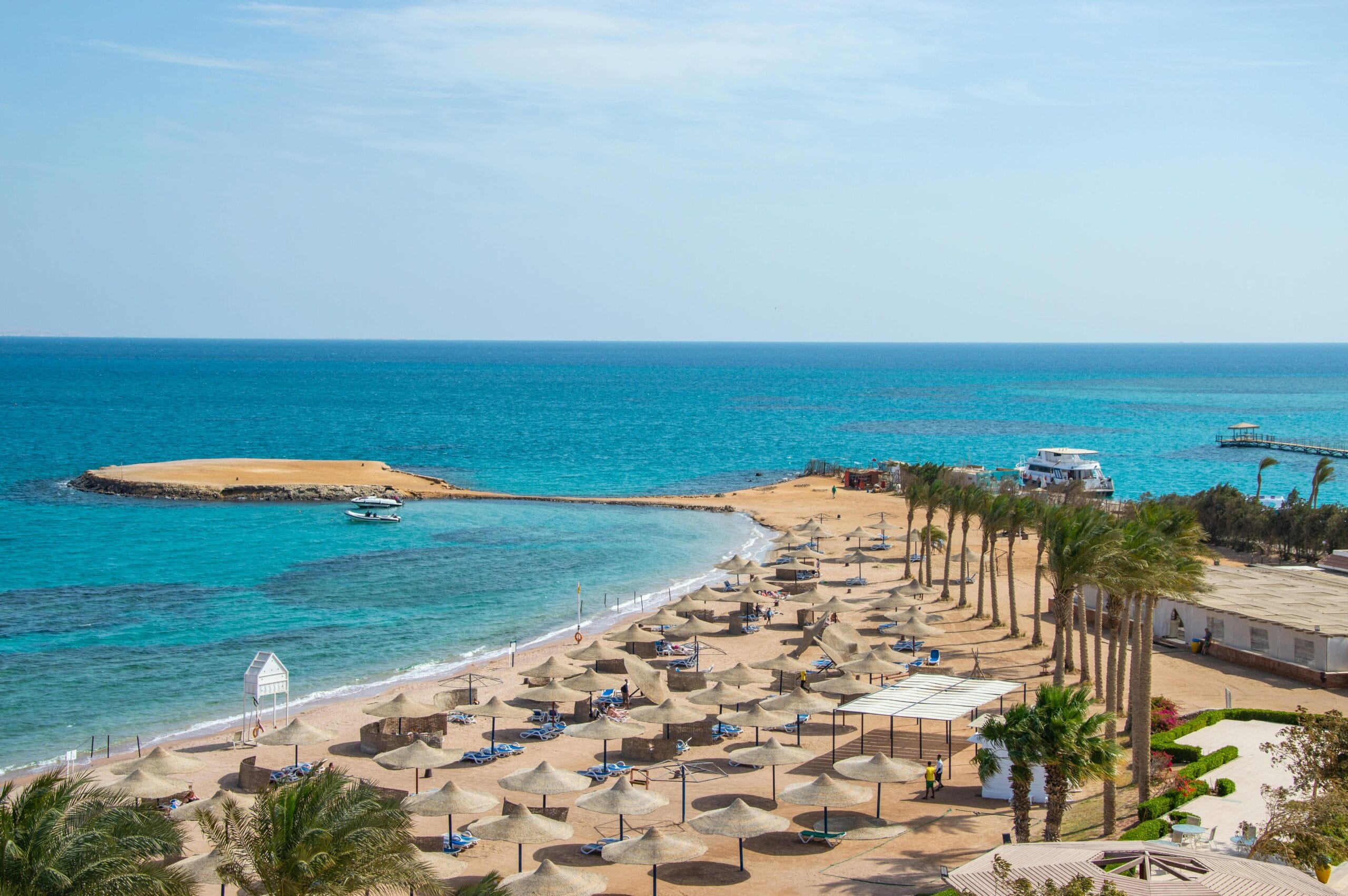 Beach resort in Hurghada Egypt with palm trees, sun umbrellas, and turquoise Red Sea water along the coastline.