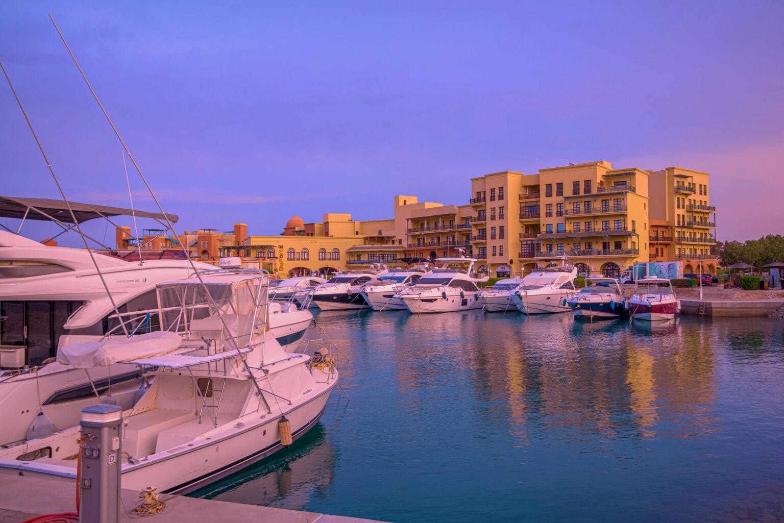 Luxury yachts docked at Hurghada Marina with waterfront hotels and colorful sunset sky along the Red Sea coast of Egypt.
